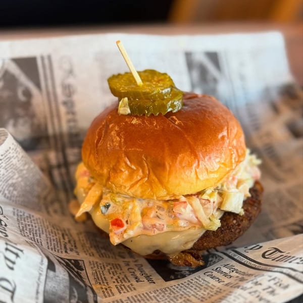 A close-up of an Island Burger and Shake burger with melted cheese, coleslaw, and a pickle on top.