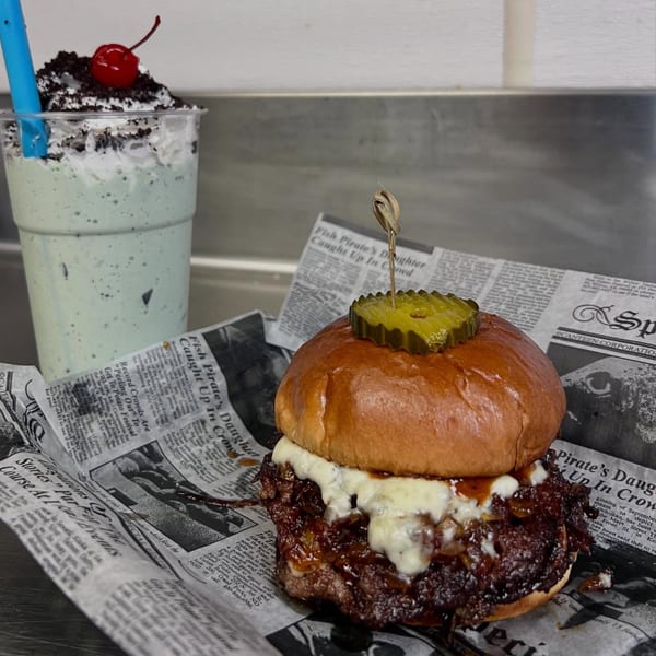 A burger with melted cheese and caramelized onions, next to a mint chocolate chip shake.