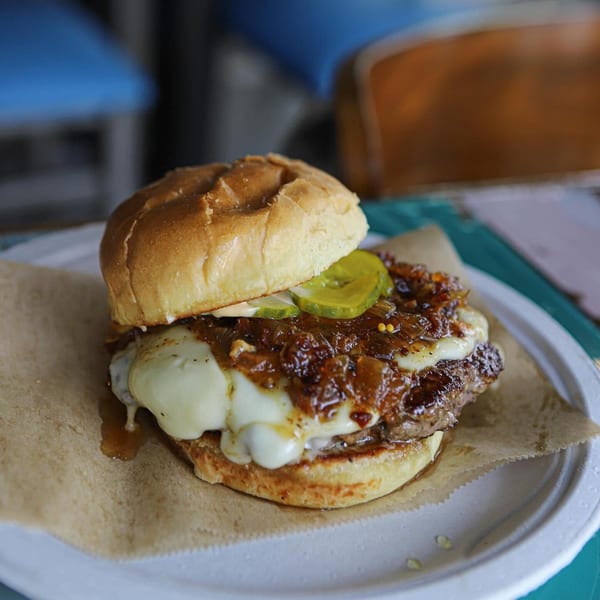 A juicy Island Burger with melted cheese, caramelized onions, and pickles on a white plate.