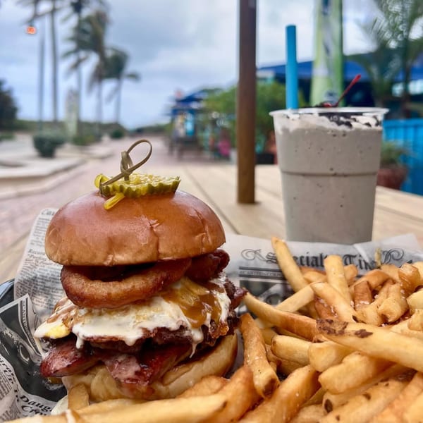 Island Burger and Shake's burger with onion rings, fried egg, bacon, fries, and milkshake outdoors.