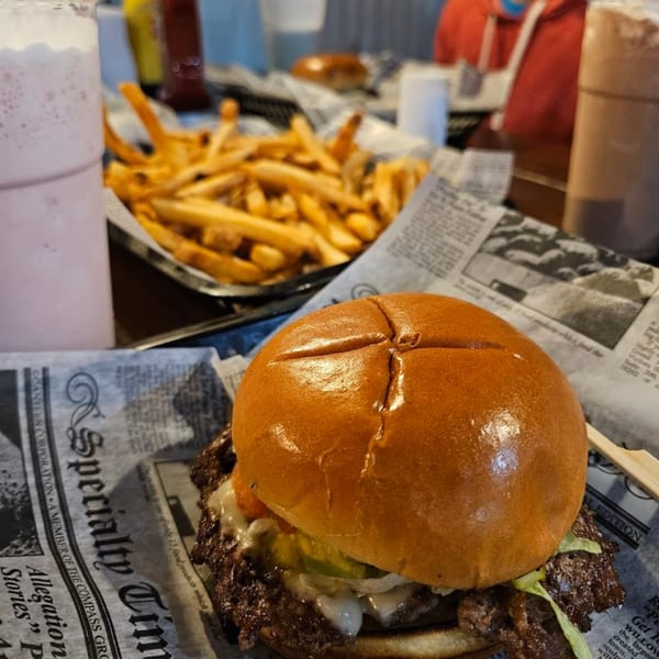 A delicious Island Burger and fries, with a pink milkshake and chocolate shake in the background.