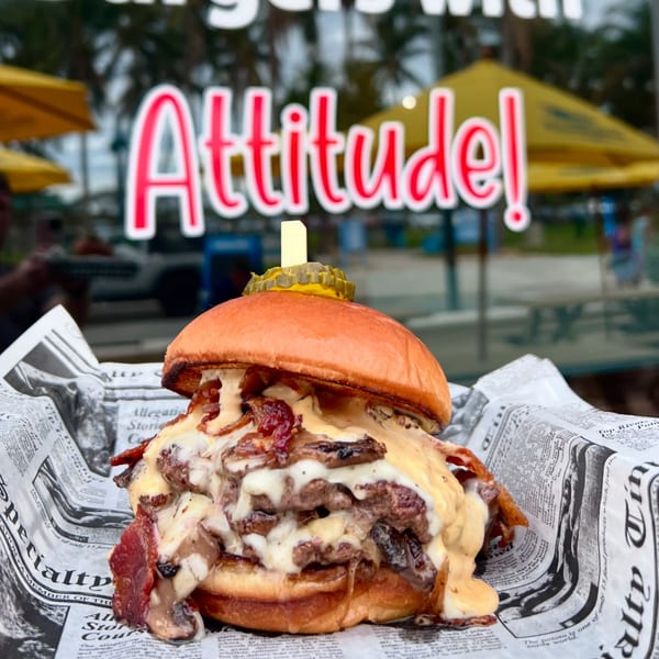 A loaded Island Burger with melted cheese, bacon, and mushrooms, wrapped in newspaper.